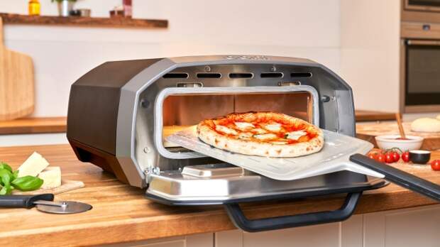 The Ooni Volt 12 electric pizza oven in a kitchen setting, with a pizza being put in the oven