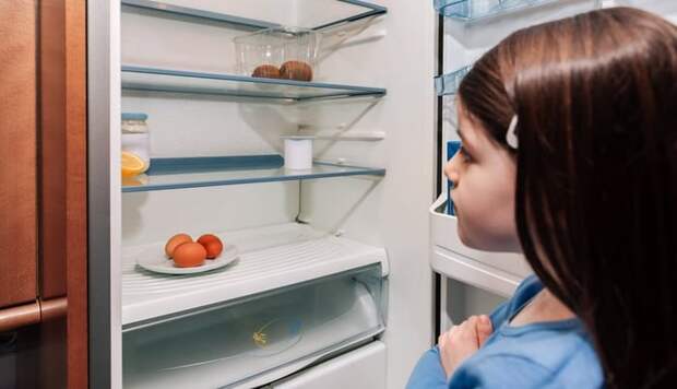 Young girl opening up refrigerator to find it mostly empty.