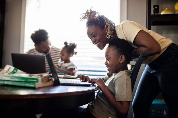 Mother helping young child with e-learning on laptop.