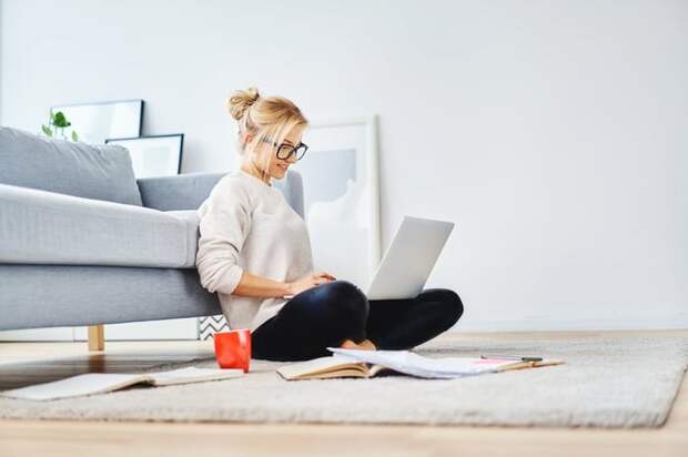 A young woman sitting on the floor working on her laptop.