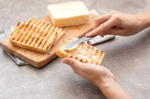 Female hand butters toasts for breakfast on the grey slate background. Horizontal view