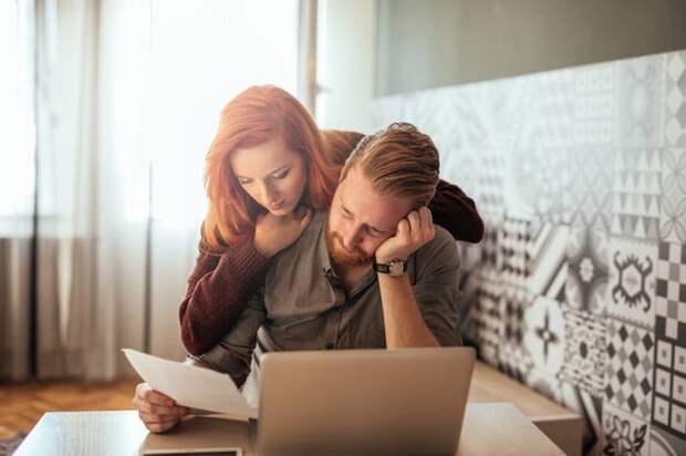 A worried couple looks at paperwork and a laptop.