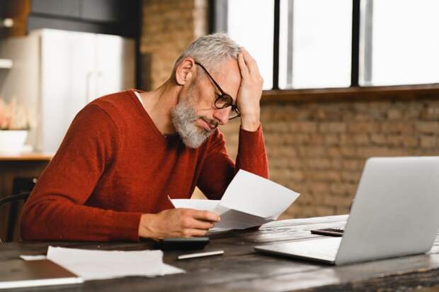A person at a laptop holding a document.