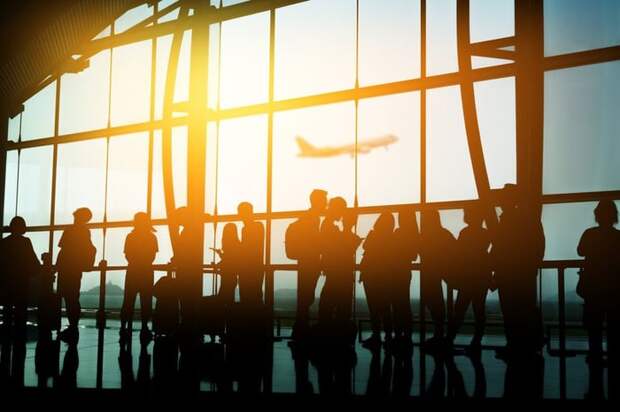 A crowd of people in front of a sunny airport window.
