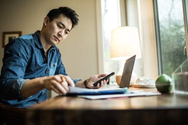 Person holding smartphone and looking at documents in office.