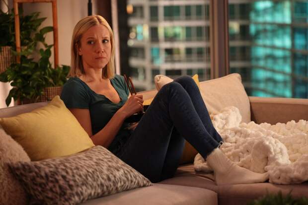Hannah sitting on her couch with her feet pulled up, wearing a green top and black pants on Chicago Med Season 10 Episode 3