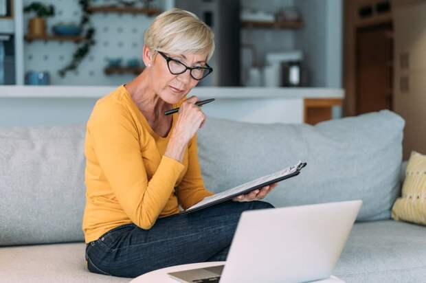 A person at a laptop holding a clipboard.