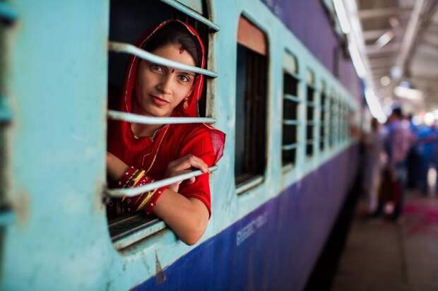 Мимолетная улыбка женщины в традиционной одежде из окна поезда, остановившегося на вокзале.
