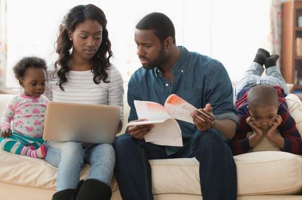 Stressed parents struggle to pay bills on a computer. They sit with their two children on a couch.