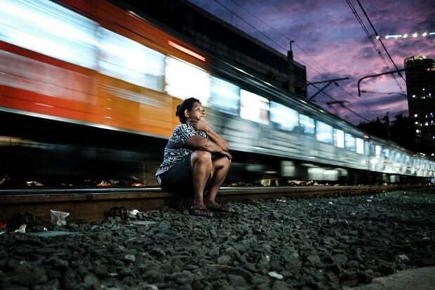 4. Женщина отдыхает, расположившись на рельсах, в то время как всего в паре метров от нее проносится поезд бедность, джакарта, железная дорога, индонезия, нищета, репортаж, трущобы
