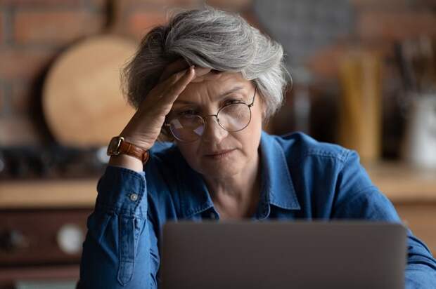 Stressed person with hand on head looking at laptop.