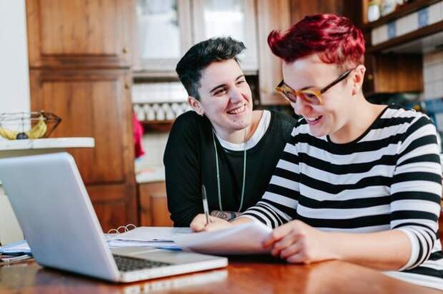 A couple smiles as they pay bills online at the kitchen table.