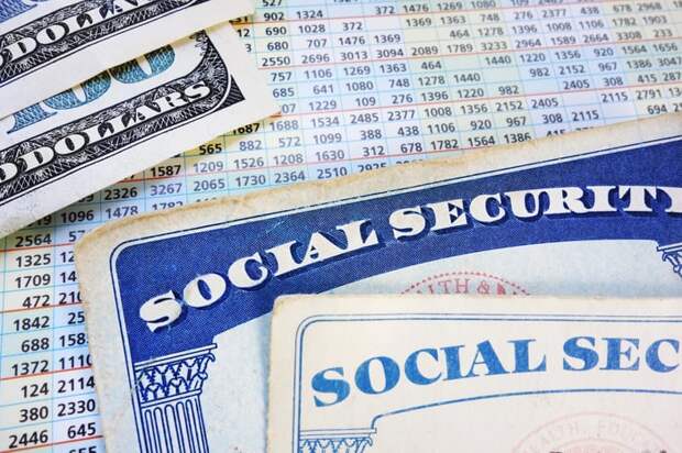Two Social Security cards and two one hundred dollar bills set atop a payout schedule sheet.