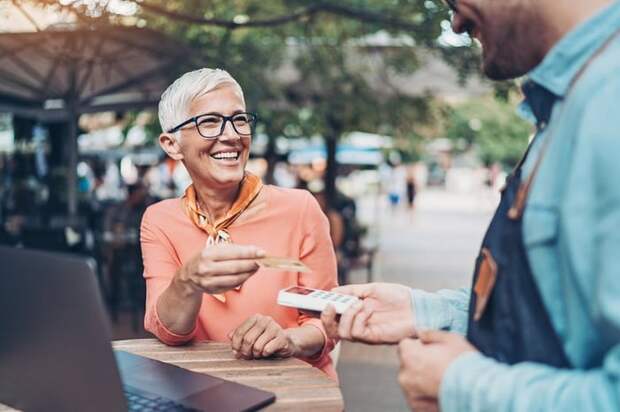 A person sitting at an outdoor table handing a credit card to a restaurant employee holding a payment reader.