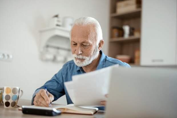 A person at a table with a laptop holding documents and a pen.