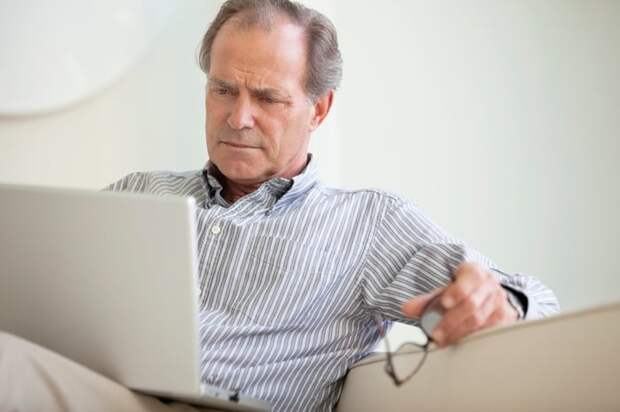 A person seated on a couch who's critically reading content from a laptop on their lap.