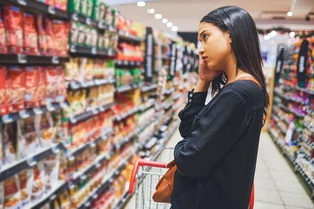 A young adult looks at a grocery store shelf concerned.