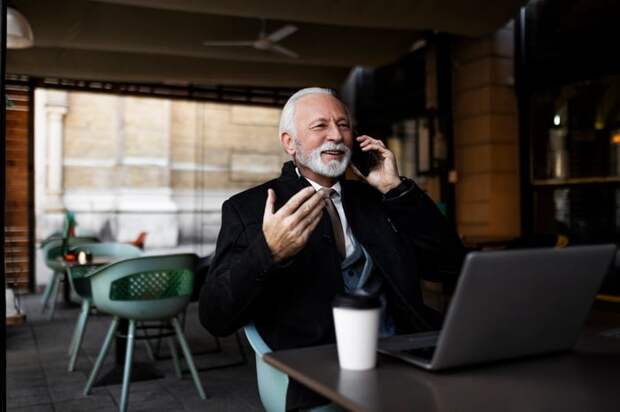 A smiling person at a laptop holding a phone.