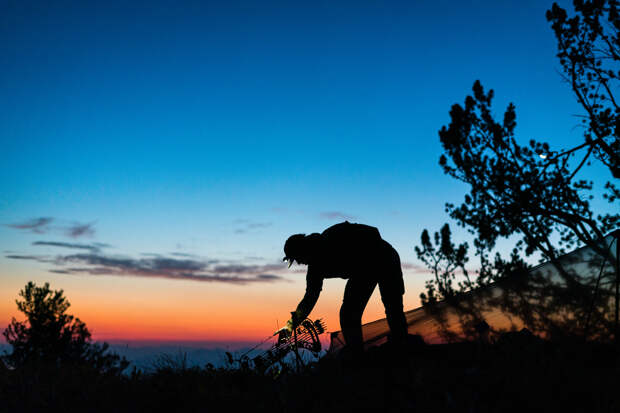 person bending over to pick up a bow as the sun sets