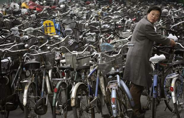 Женщина забирает свой велосипед с велопарковки у станции метро в Пекине. китай, люди, население