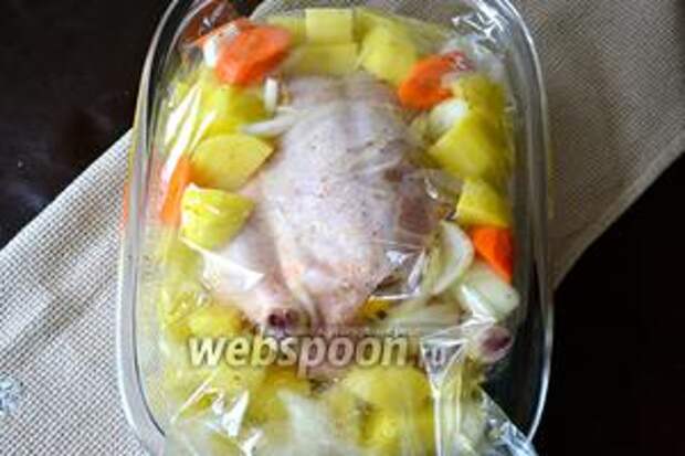 В жаростойкую форму для запекания положить пакет для запекания, вложить внутрь цыплёнка, а вокруг него выложить овощи.