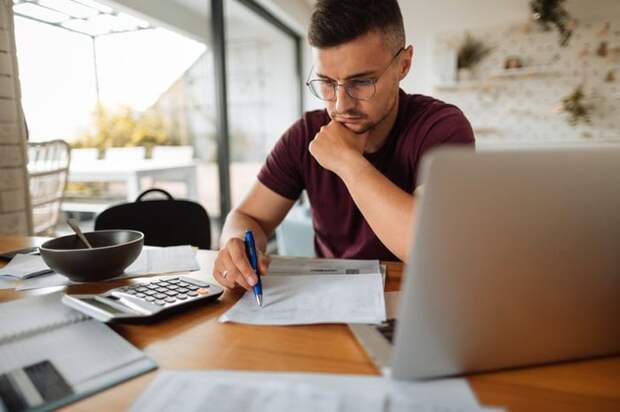 A man looking stressed while going through his bills next to his open laptop.