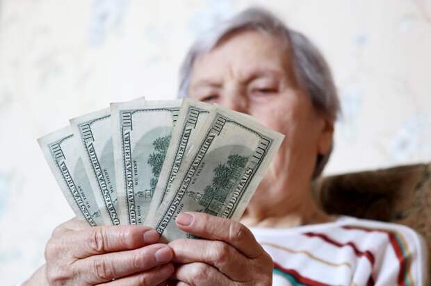 A seated person counting a fanned pile of one-hundred-dollar bills in their hands.