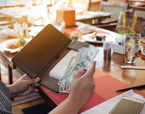 A woman placing cash in a check folder while sitting at a table in a restaurant.