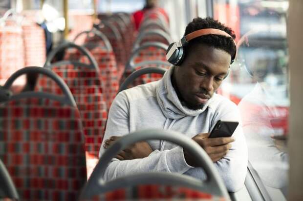 A man riding the bus and listening to music while looking at his phone.