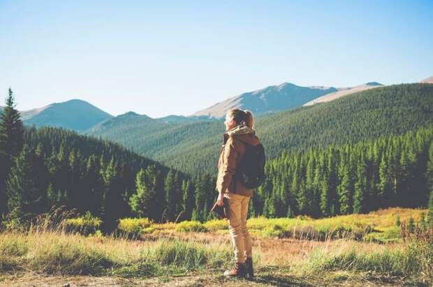 A hiker standing at the top of an open space and admiring the view of the mountains and trees.
