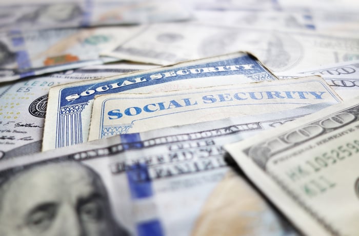 Two Social Security cards set within a messy pile of one hundred dollar bills.