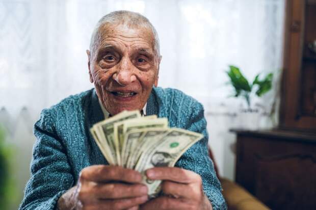 A smiling person who's sitting down and counting a fanned assortment of cash bills in their hands.