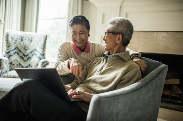 Smiling couple sitting in living room looking at laptop.