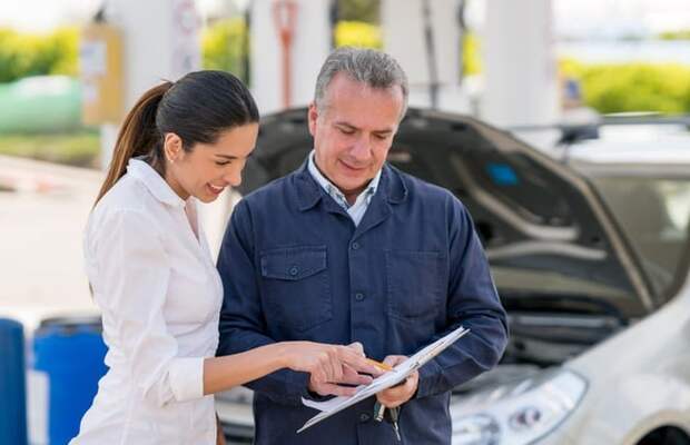 Young woman at a garage talking to a mechanic about her car. They both point at paperwork.