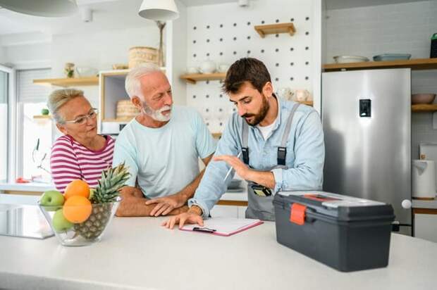 A repairman speaking with an older man and woman in their kitchen.