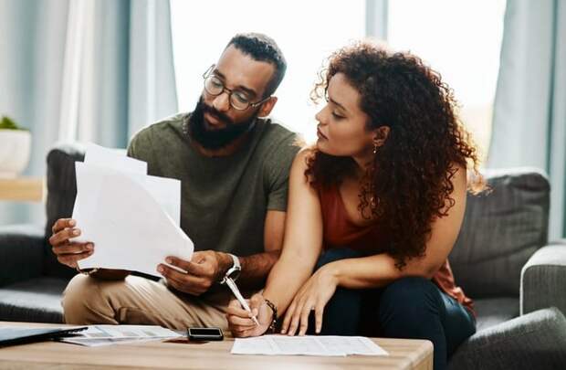 A man and woman sitting on their couch looking through bills and signing papers.