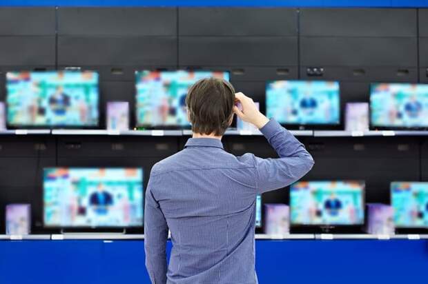 A man standing in front of a wall of TVs in an electronics store.