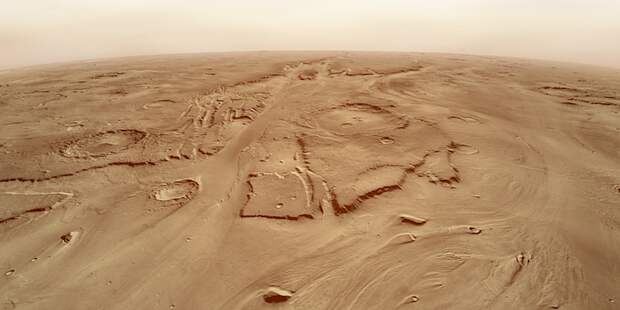 A landscape of sepia orange ground with long grooves in it stretches towards a dusty horizon.