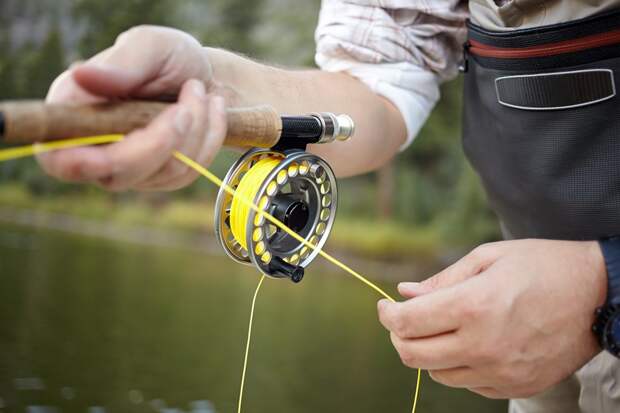 A close-up of a fly fisherman's hands as he pulls line on his reel