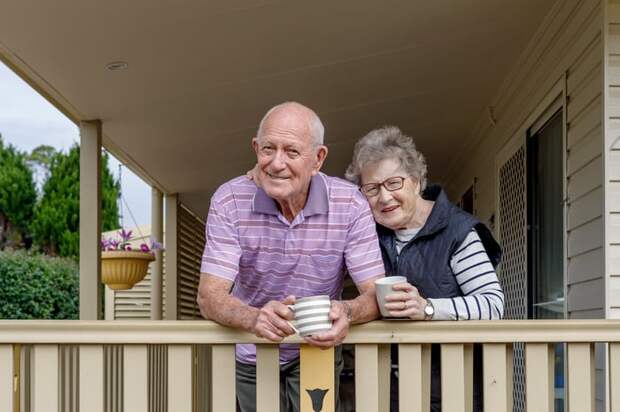 Two people with cups stand on a porch.