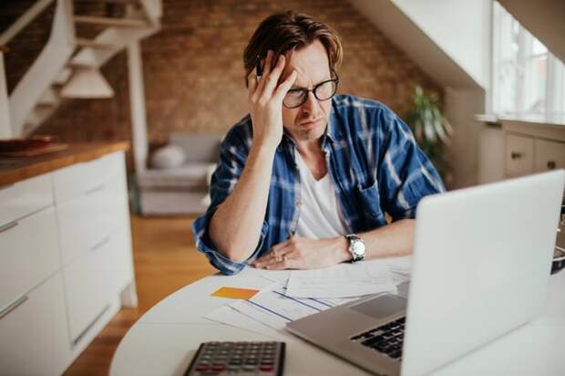 Person with hand on head looking at laptop.