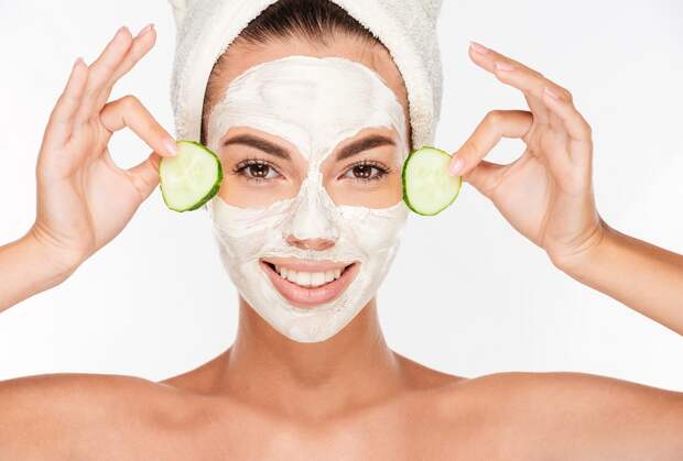 Beautiful woman applying cucumber on her face with cosmetic mask isolated on white background