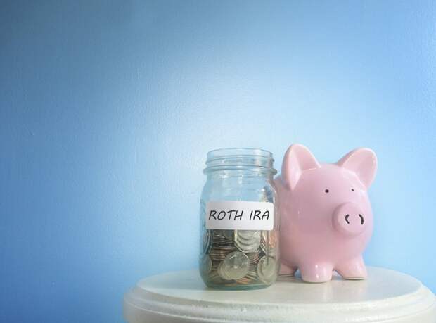 Pink piggy bank sitting next to jar that says ROTH IRA on a beige table.