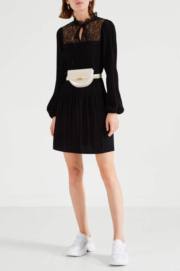 Маленькое черное плиссированное платье Maje приталенного кроя с длинными объемными рукавами. В верхней части – кружевная вставка, кружевной воротник. К платью подобраны белые кроссовки на толстой подошве.