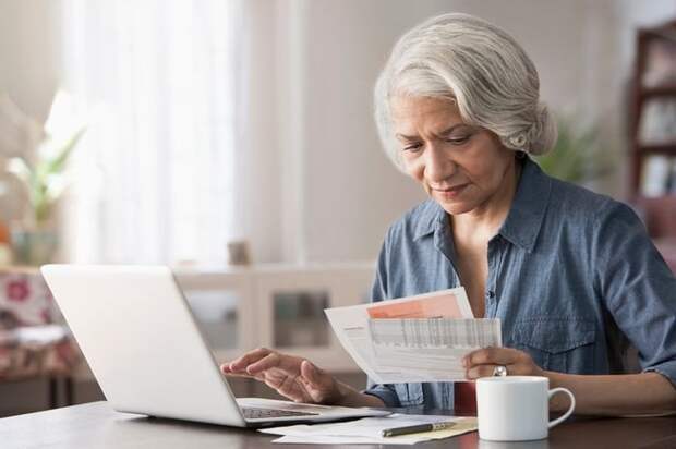 An older person pays bills using their laptop at home.