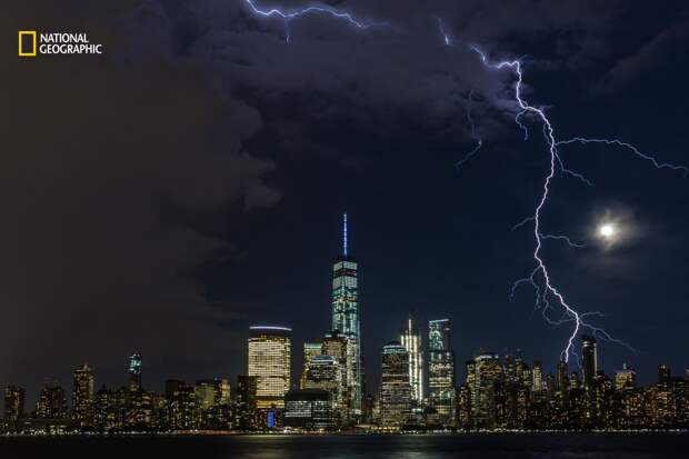 Lightning strikes lower Manhattan as a summer storm approaches a moonlit New York City skyline.