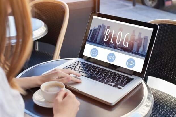 A woman at a coffee shop reads a blog on her laptop