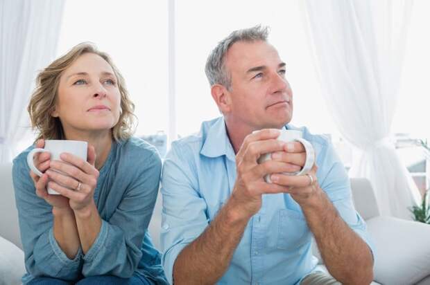 A couple holding coffee mugs and sitting together on a couch.