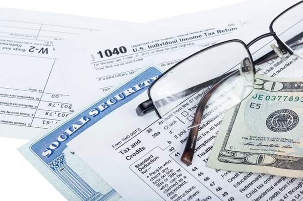 A pair of glasses, a twenty dollar bill, and a Social Security card set atop IRS tax forms.