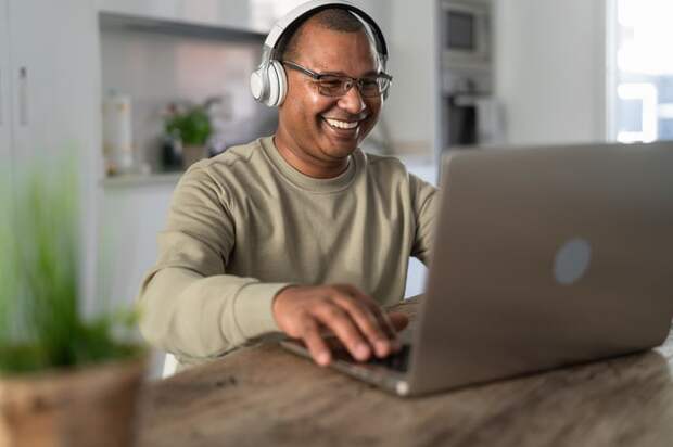 A smiling person at a laptop wearing headphones.